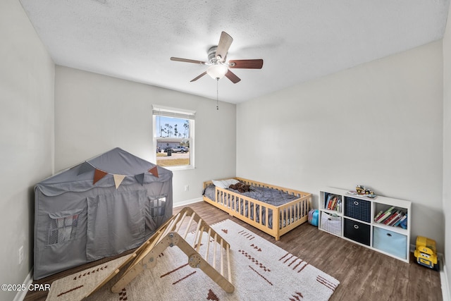 bedroom featuring ceiling fan, a textured ceiling, baseboards, and wood finished floors