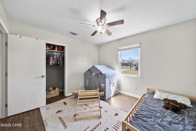 bedroom featuring baseboards, visible vents, wood finished floors, a textured ceiling, and a closet