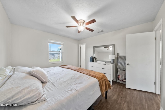 bedroom with dark wood-style floors, a textured ceiling, visible vents, and a ceiling fan