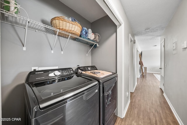 washroom with a textured ceiling, separate washer and dryer, wood finished floors, laundry area, and baseboards