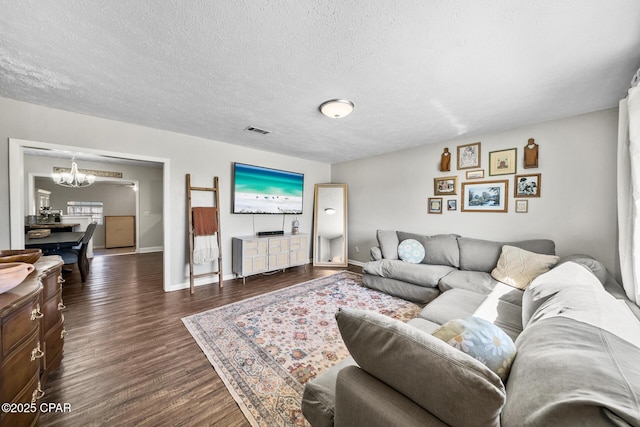 living area featuring a textured ceiling, a notable chandelier, visible vents, baseboards, and dark wood finished floors