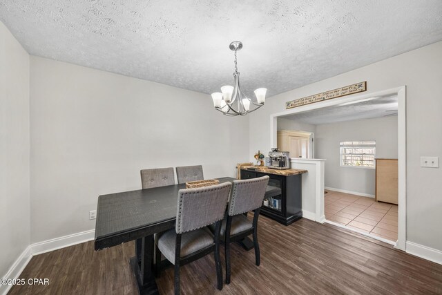 dining room with a chandelier, dark wood-style flooring, a textured ceiling, and baseboards