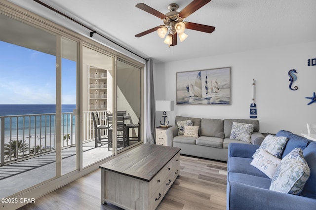 living area with a water view, light wood-style floors, ceiling fan, and a beach view