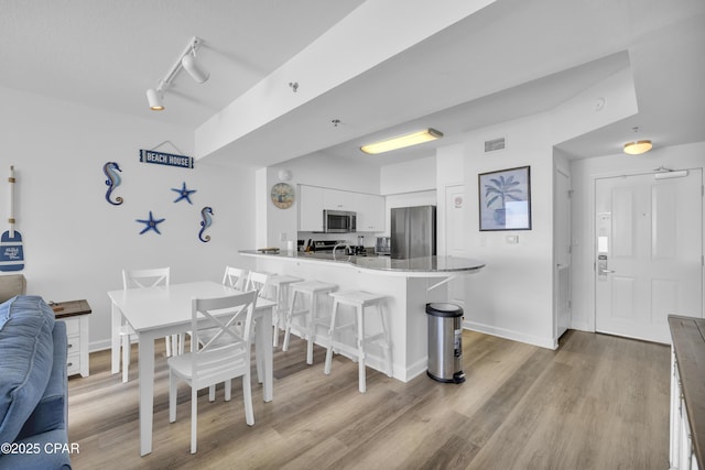 dining space with light wood-type flooring, rail lighting, baseboards, and visible vents