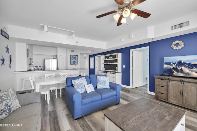 living area with ceiling fan, wood finished floors, visible vents, baseboards, and track lighting