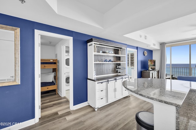 kitchen featuring stacked washer / drying machine, baseboards, white cabinetry, and light wood finished floors