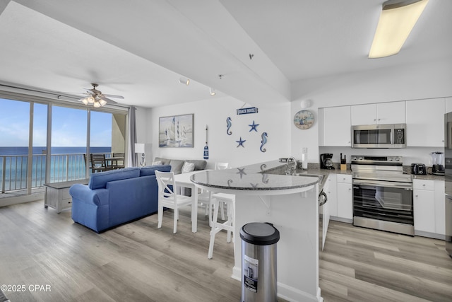 kitchen featuring a breakfast bar, appliances with stainless steel finishes, white cabinets, a sink, and a peninsula