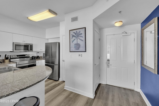 kitchen with visible vents, white cabinets, light wood-style flooring, appliances with stainless steel finishes, and a sink