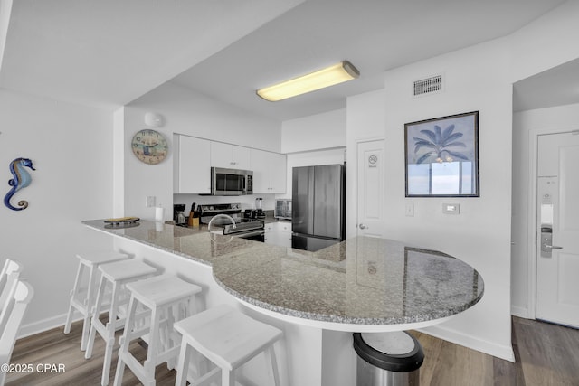 kitchen with visible vents, appliances with stainless steel finishes, white cabinetry, wood finished floors, and a peninsula