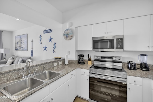 kitchen with stainless steel appliances, open floor plan, white cabinets, a sink, and a peninsula