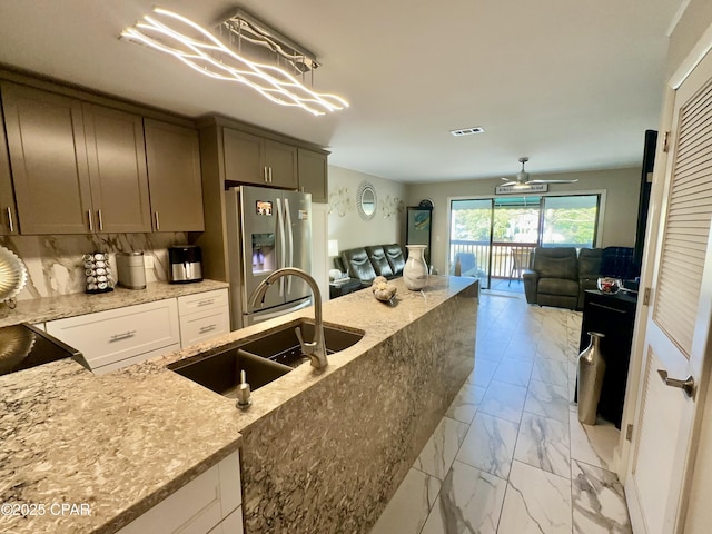 kitchen featuring light stone counters, a sink, stainless steel refrigerator with ice dispenser, marble finish floor, and open floor plan