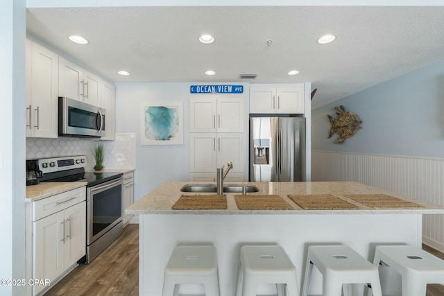 12011 Front Beach Rd Unit 204B, Panama City Beach, FL 32407 - kitchen with appliances with stainless steel finishes, a sink, wood finished floors, a breakfast bar area, and wainscoting