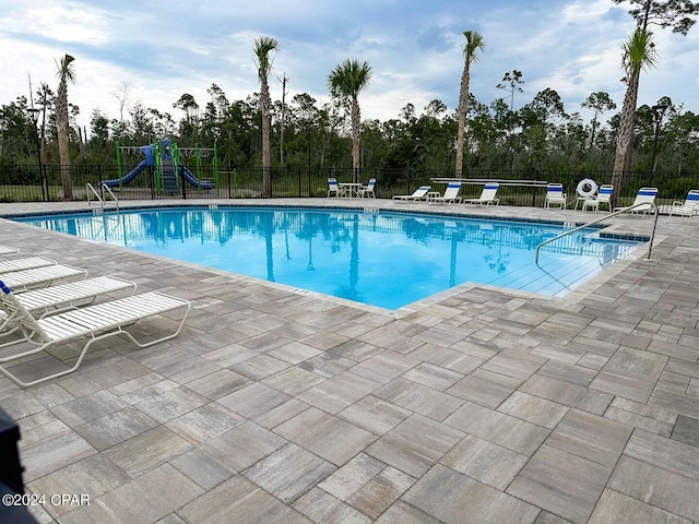 pool featuring a patio, playground community, and fence