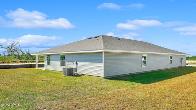 view of side of property with a shingled roof, central AC, and a yard