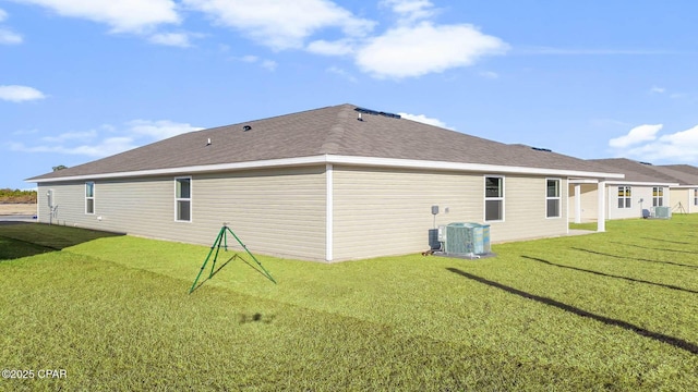 back of property featuring a shingled roof, cooling unit, and a yard