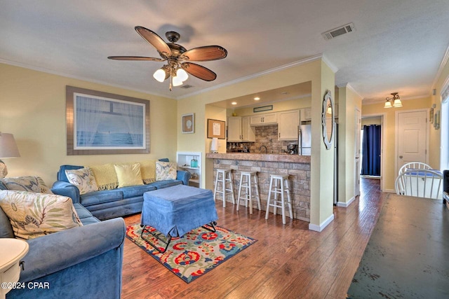 living area featuring ceiling fan, wood finished floors, visible vents, baseboards, and crown molding