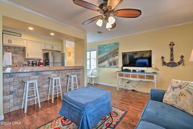 living area featuring wood finished floors, visible vents, baseboards, a ceiling fan, and ornamental molding