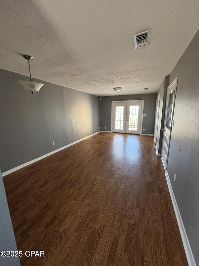 unfurnished room with french doors, dark wood finished floors, visible vents, a textured ceiling, and baseboards