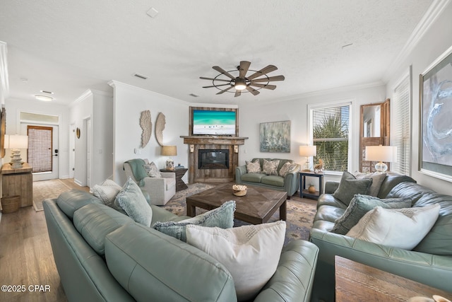 living area with visible vents, a textured ceiling, a glass covered fireplace, wood finished floors, and crown molding