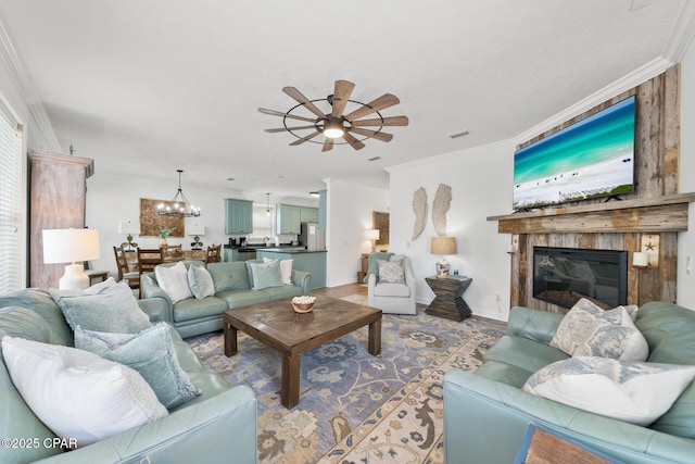 living room featuring ceiling fan with notable chandelier, a large fireplace, crown molding, light wood finished floors, and baseboards