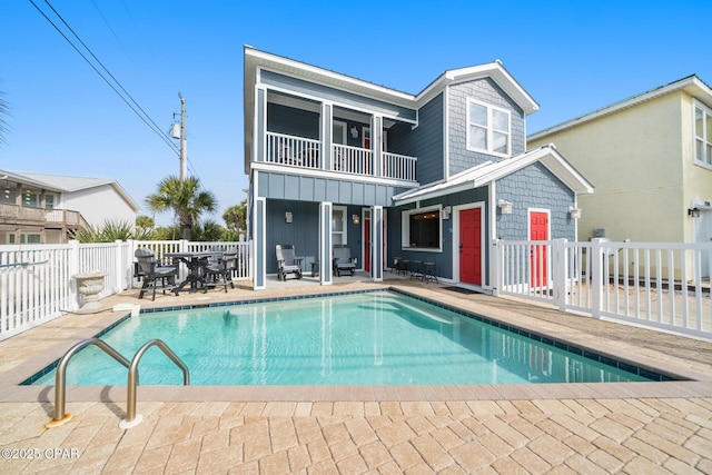 back of property featuring a patio, fence, board and batten siding, a fenced in pool, and a balcony