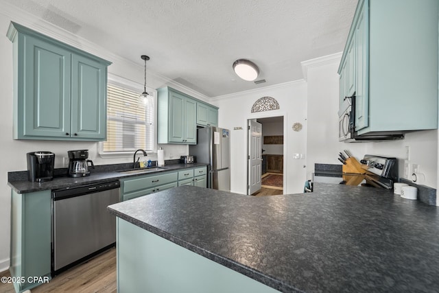 kitchen featuring a peninsula, a sink, ornamental molding, stainless steel appliances, and dark countertops