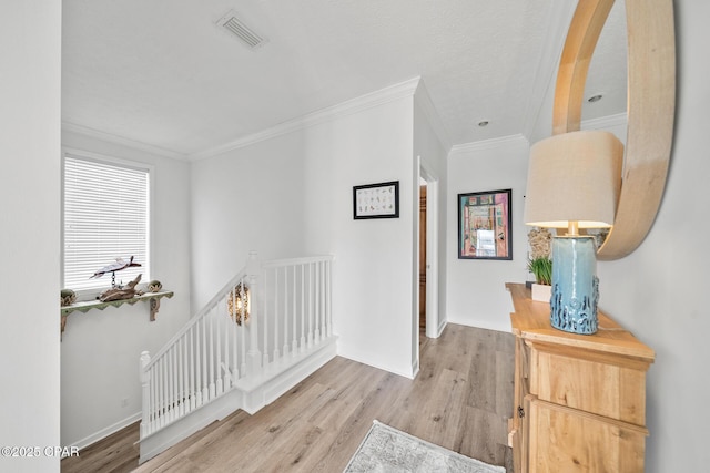 hallway with light wood-type flooring, an upstairs landing, visible vents, ornamental molding, and baseboards