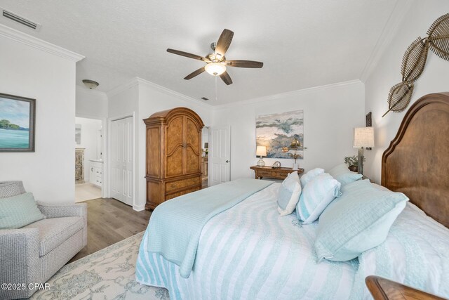 bedroom with visible vents, a ceiling fan, ensuite bath, wood finished floors, and crown molding