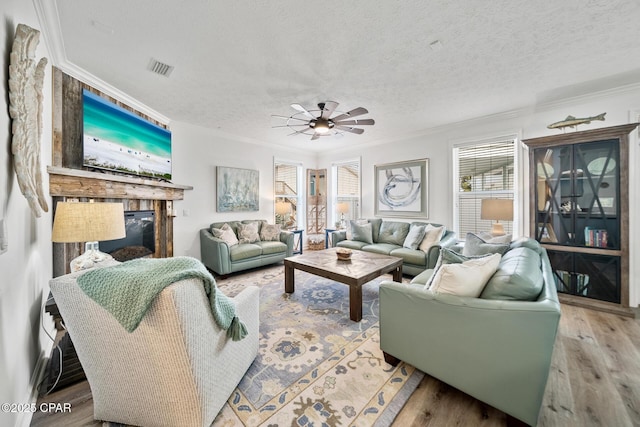 living area with a glass covered fireplace, a textured ceiling, wood finished floors, and ornamental molding