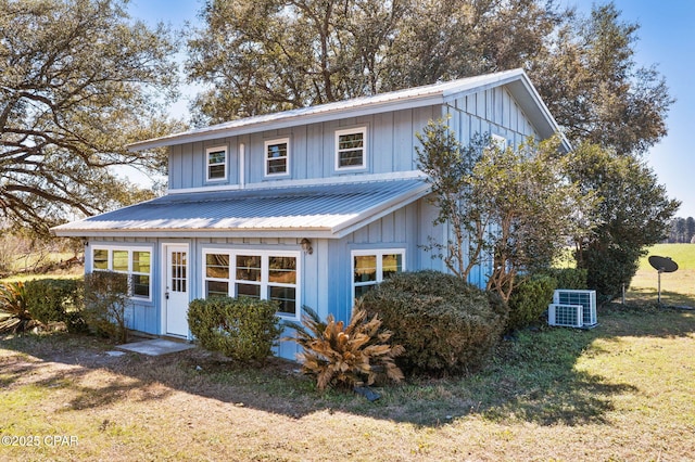 view of front facade with cooling unit, metal roof, board and batten siding, and a front yard