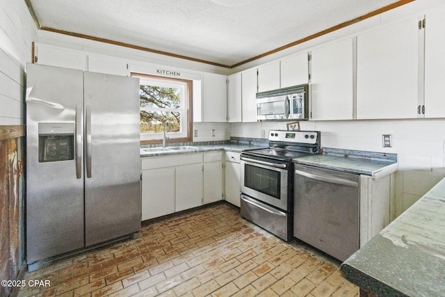 kitchen featuring stainless steel appliances, brick floor, white cabinetry, and a sink