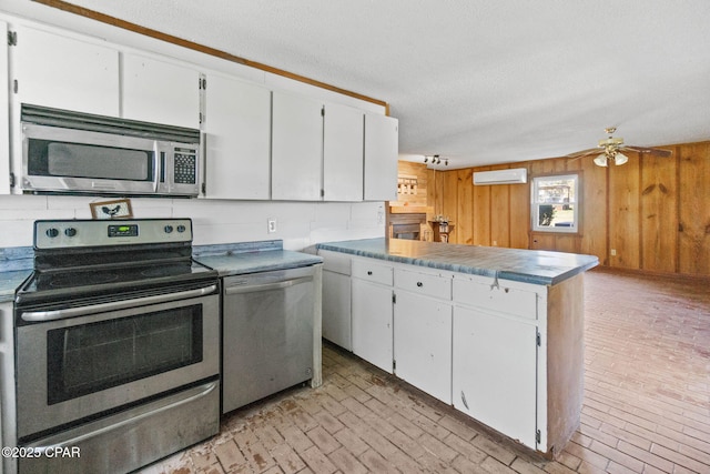 kitchen with appliances with stainless steel finishes, white cabinets, a wall unit AC, and a peninsula