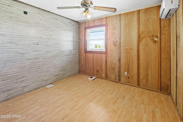 spare room featuring an AC wall unit, ceiling fan, wood walls, a textured ceiling, and wood finished floors