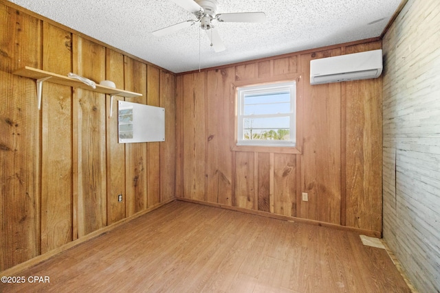 unfurnished room with a textured ceiling, an AC wall unit, ceiling fan, and wood finished floors