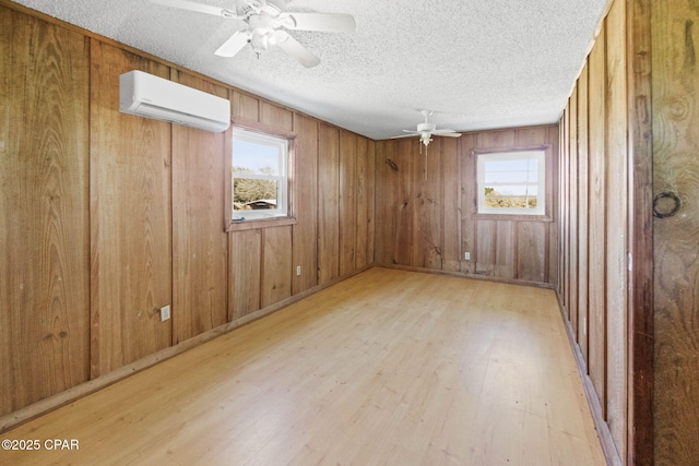 empty room with ceiling fan, plenty of natural light, light wood-style flooring, and a wall mounted AC