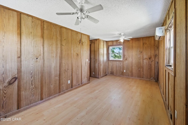 spare room featuring wooden walls, a ceiling fan, wood finished floors, a wall mounted air conditioner, and a textured ceiling