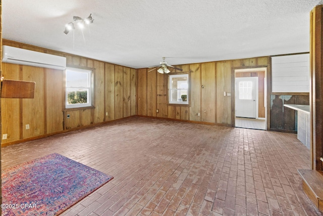 unfurnished living room featuring brick floor, a wall mounted air conditioner, ceiling fan, and wooden walls