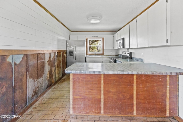 kitchen with wooden walls, a peninsula, a sink, appliances with stainless steel finishes, and crown molding