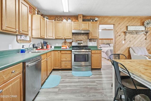 kitchen featuring a textured ceiling, light wood-style floors, under cabinet range hood, wood walls, and appliances with stainless steel finishes