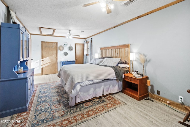 bedroom featuring light wood finished floors, visible vents, a textured ceiling, and ornamental molding