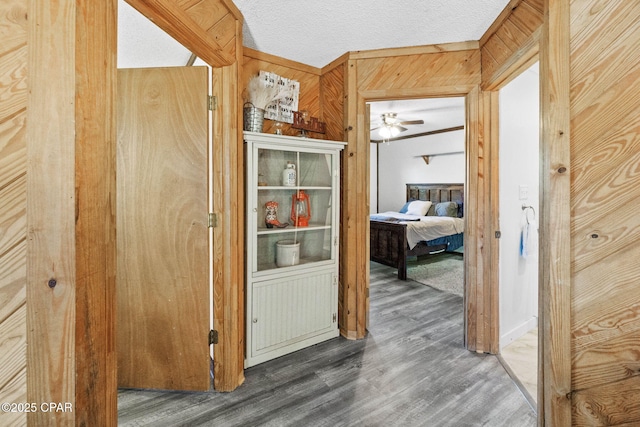 hall with wooden walls, a textured ceiling, and wood finished floors