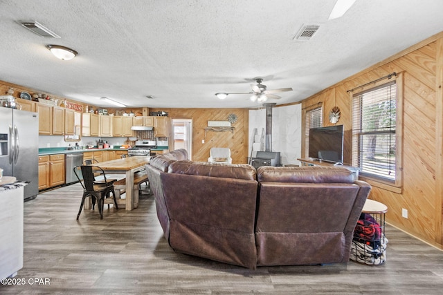 living room featuring a wood stove, wooden walls, light wood-style flooring, and visible vents