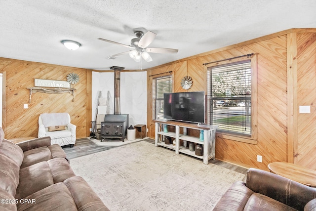 living area with wooden walls, wood finished floors, a wood stove, and a textured ceiling