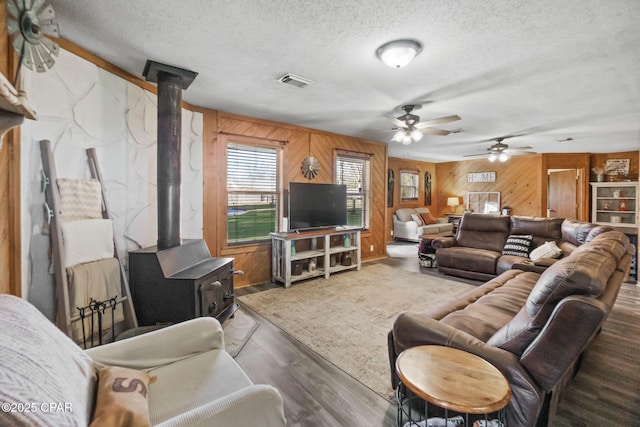 living room featuring visible vents, a textured ceiling, wood finished floors, and a wood stove