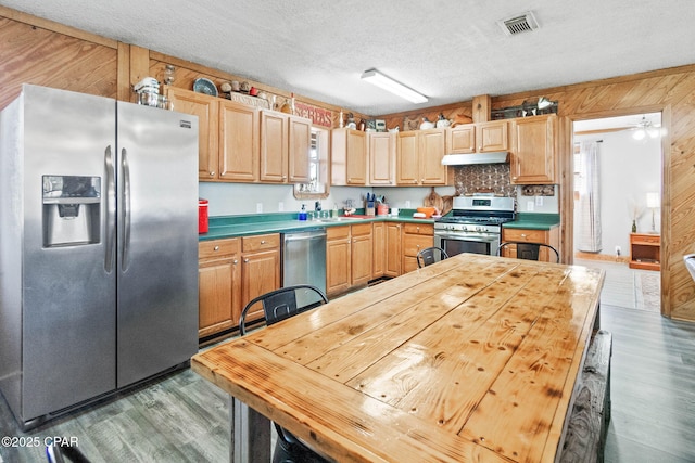 kitchen featuring wooden walls, wood finished floors, visible vents, appliances with stainless steel finishes, and a textured ceiling