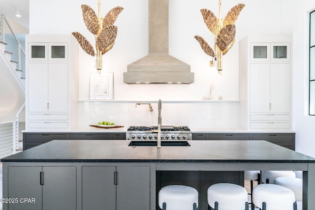 kitchen featuring a center island with sink, wall chimney exhaust hood, glass insert cabinets, a breakfast bar, and gray cabinets