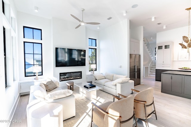 living room with visible vents, a glass covered fireplace, a towering ceiling, light wood-style flooring, and stairway