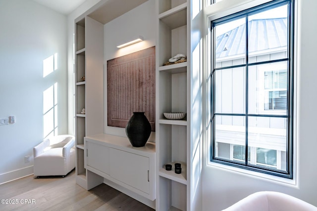 living area with built in shelves, baseboards, a healthy amount of sunlight, and light wood finished floors