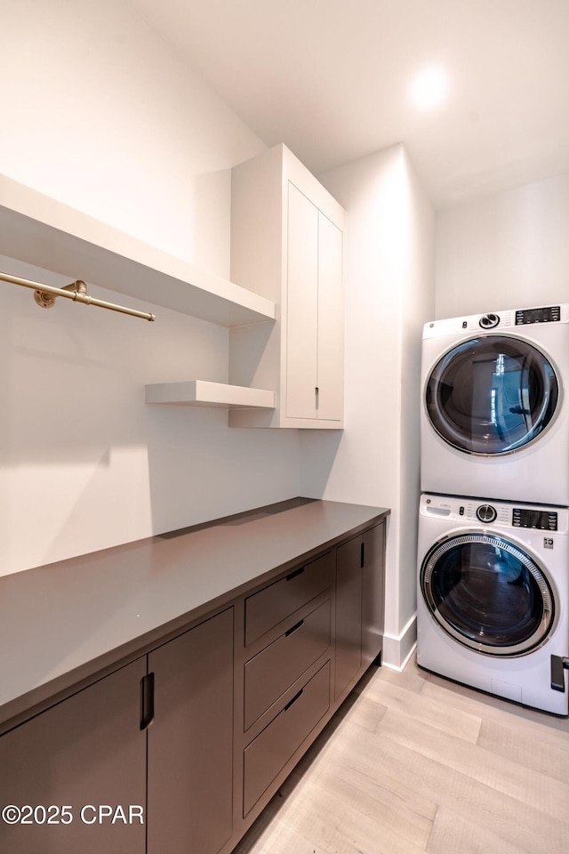 clothes washing area featuring cabinet space, light wood-style flooring, and stacked washing maching and dryer