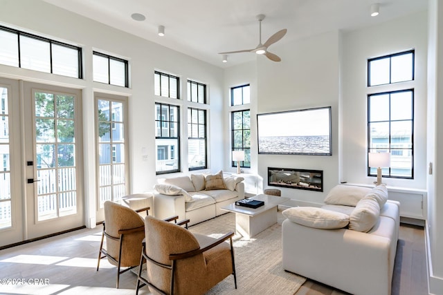 living area featuring light wood-type flooring, a wealth of natural light, a glass covered fireplace, and a towering ceiling